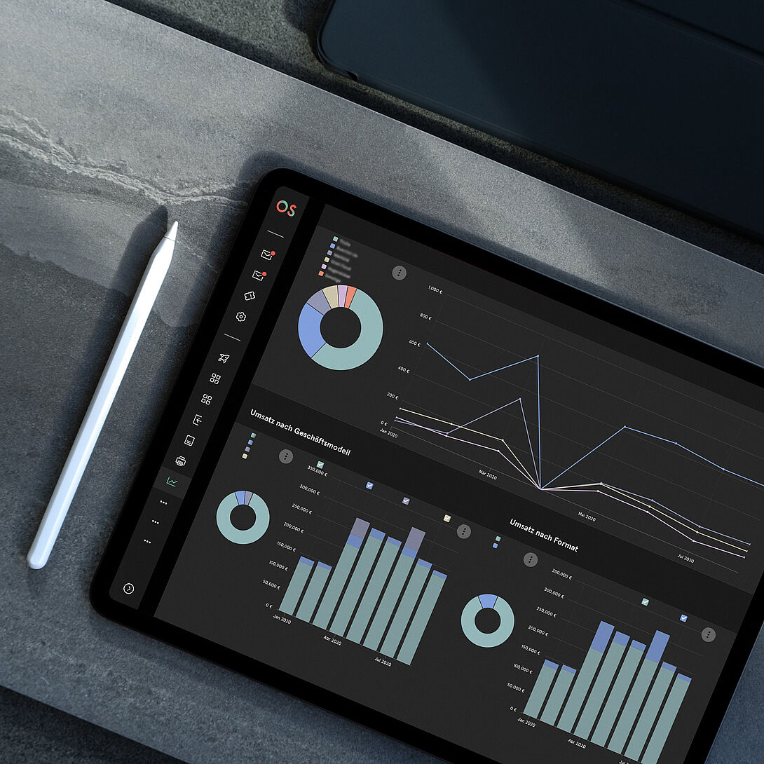 Tablet on a work surface displays an analytics dashboard with charts and key figures on revenue, sales, and performance, with a stylus next to it.